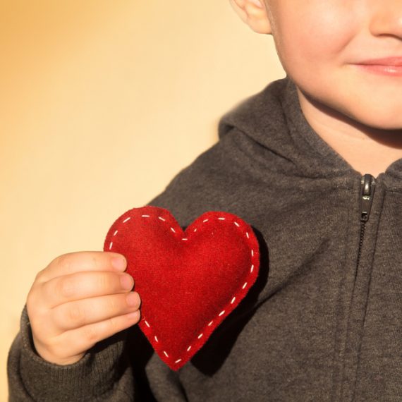 Red heart in child hands. Kindness concept, gift, hand made valentine, close up.