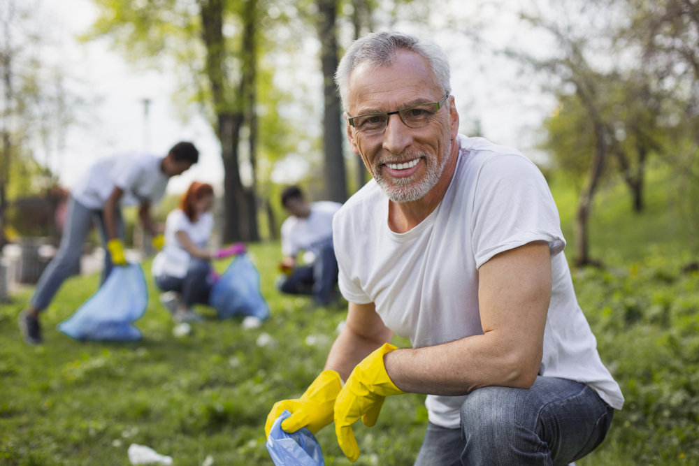 Work as volunteer. Experienced senior volunteer holding garbage bag and staring at camera