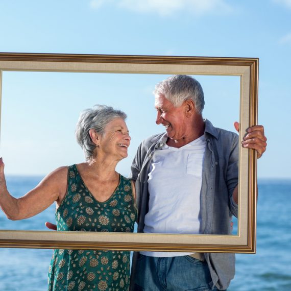 Senior couple posing with a frame on the beach