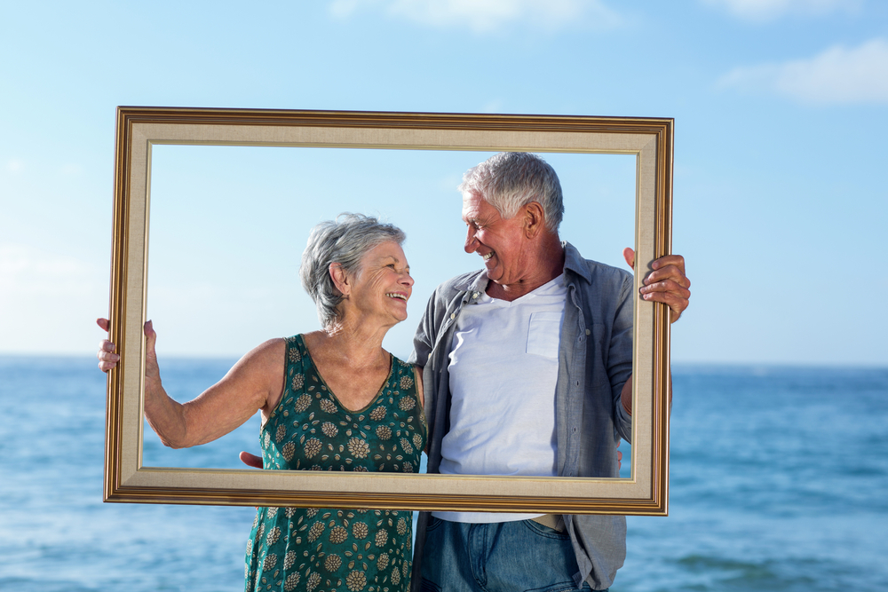 Senior couple posing with a frame on the beach